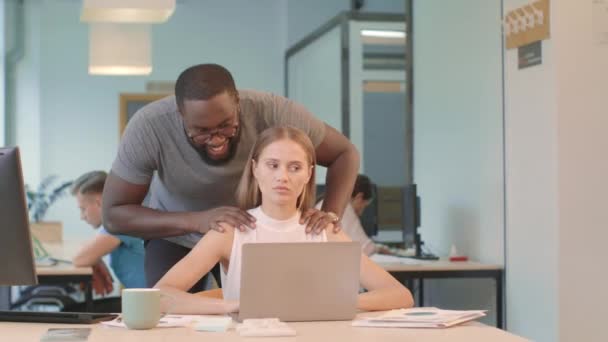 Una mujer guapa trabajando en la computadora en el coworking. negro hombre haciendo masaje — Vídeo de stock