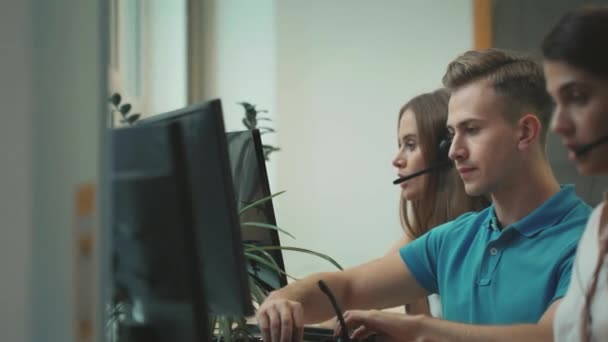 Mladý operátor dává náhlavní soupravu do call centra. Usměvavý muž mluvící s klientem — Stock video