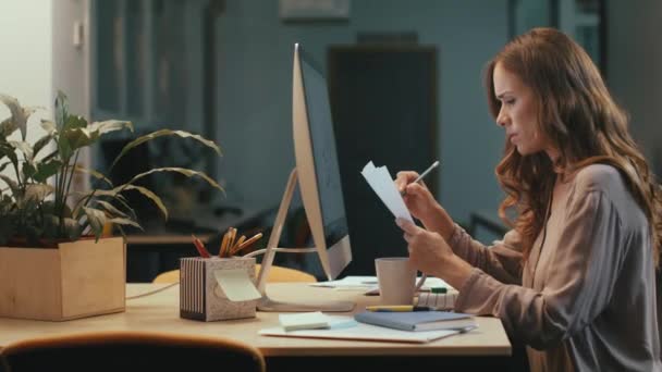 Mujer de negocios enfocada que trabaja con gráficos financieros en la pantalla de la computadora por la noche — Vídeo de stock