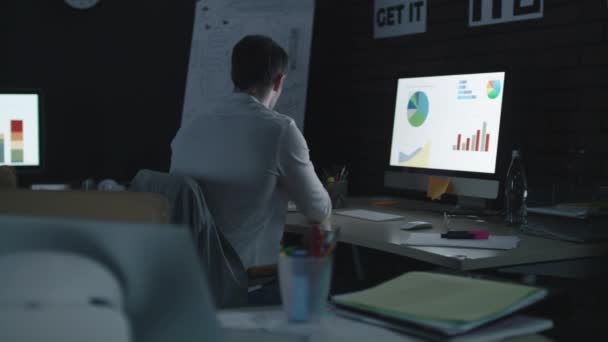 Hombre de negocios sobrecargado analizando gráfico financiero y diagrama en la oficina nocturna — Vídeo de stock