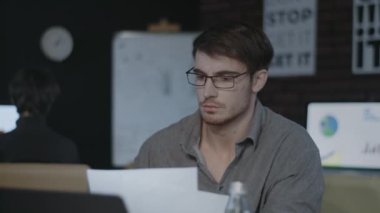 Konsantre iş analisti karanlık ofiste belge ve dizüstü bilgisayar izliyor.