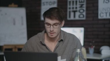 Karanlık ofiste dizüstü bilgisayarın yanında çalışan konsantre bir iş adamı.