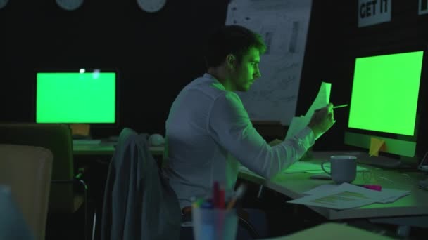 Young businessman working on computer with green monitor in night office. — Stock Video