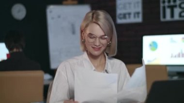 Tatmin olmuş bir iş kadını karanlık ofiste dizüstü bilgisayarla iyi sonuçlar alıyor.