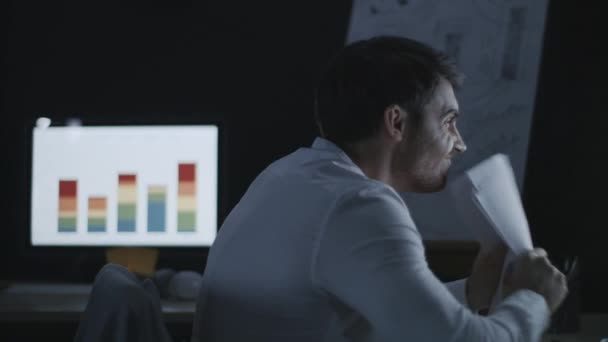 Hombre de negocios enojado tirando papel de documento en la mesa de la computadora en la oficina oscura — Vídeo de stock