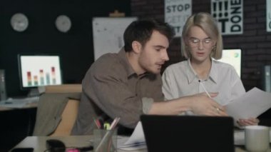 İş çifti karanlık işyerinde mali raporları tartışıyor.