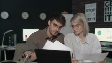 Genç iş adamı ve kadın karanlık ofiste birlikte çalışıyorlar.