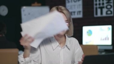 Mutsuz iş kadını, gece ofisindeki masaya kağıt atıyor.