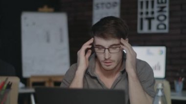 Yorgun bir iş adamı karanlık ofiste kafasına dokunuyor. Üzgün adam dizüstü bilgisayarla çok çalışıyor..