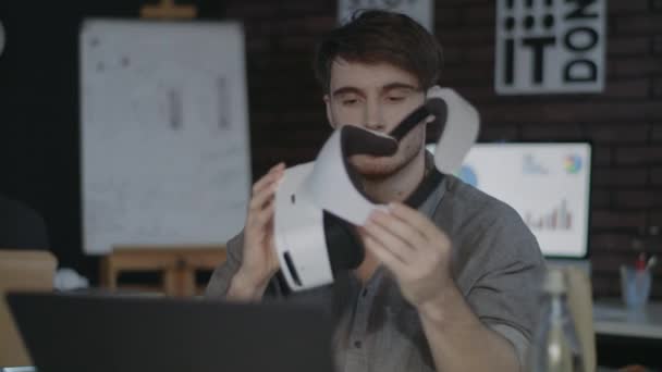 Молодой человек держит очки виртуальной реальности в креативном темном кабинете — стоковое видео