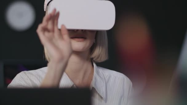 Femme souriante testant un programme informatique dans des lunettes de réalité virtuelle dans un bureau sombre — Video