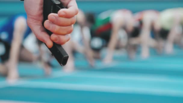 Referees hand with starting pistol on blurred background of athletes — Stock Video