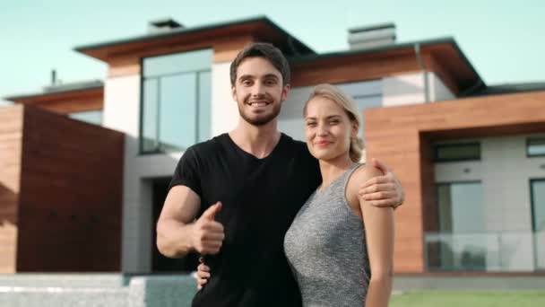 Щаслива пара робить великі пальці вгору жест біля розкішного будинку . — стокове відео