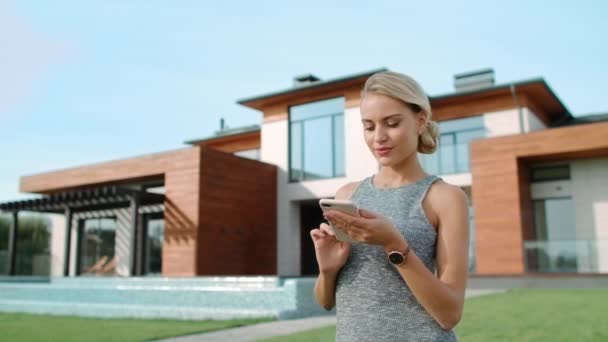 Krásná žena, která se při psaní mobilu nachází poblíž luxusní budovy. Úspěšný životní styl — Stock video