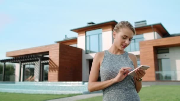 Uvolněná žena s mobilním domem poblíž luxusního domu. Krásná žena stojící blízko Villy — Stock video