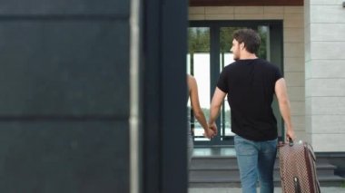 Otel arka görünümüne giren gezgin çift. Modern çift çanta ile eve geliyor