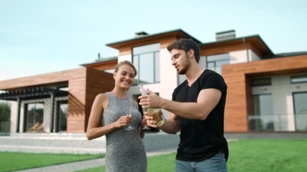 Багатий чоловік відкриває пляшкове шампанське біля будинку. Захоплена пара святкує надворі — стокове відео