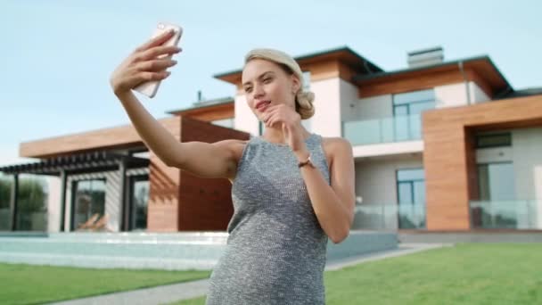 Mujer sonriente haciendo selfie cerca del apartamento. Primeros planos mujer rubia tomando fotos — Vídeos de Stock