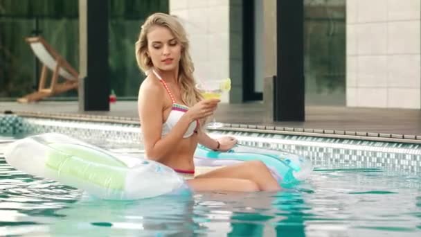 Mooie vrouw drinken cocktail op opblaasbare matras in zwembad. — Stockvideo