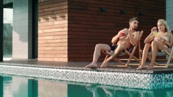 Χαρούμενο ζευγάρι που χαλαρώνει στις καρέκλες κοντά στην πισίνα στο πολυτελές σπίτι. — Αρχείο Βίντεο