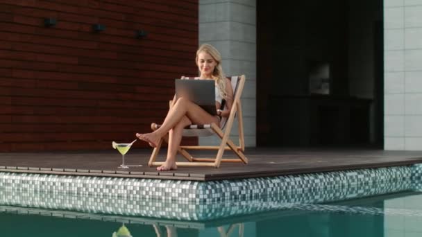 Hermosa mujer que trabaja en el ordenador portátil cerca de la piscina . — Vídeos de Stock