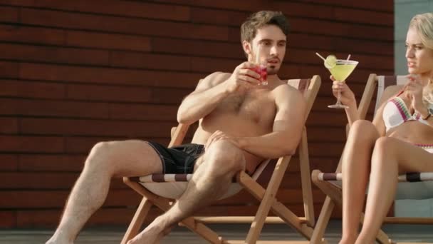 Επιτυχημένο ζευγάρι πίνοντας κοκτέιλ στις ηλιόλουστες καρέκλες κοντά στην πισίνα πολυτελείας. — Αρχείο Βίντεο