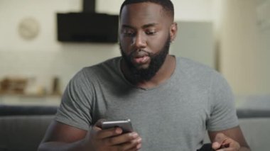 Siyah adam açık mutfakta telefon tutuyor. Akıllı telefonda manifatura konsantre adam.