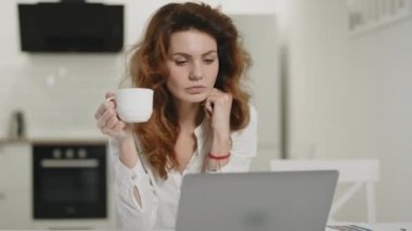 Açık mutfakta çalışan laptop odaklı kadın. Genç Bayan kahve içme