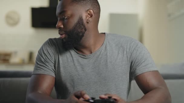 Svart man spelar video spel hemma. Upprörd kille sitter med Play Station. — Stockvideo