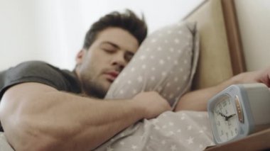 Uykucu adam sabah uyanıyor. Çalar saate bakarak rahatlatıcı adam.