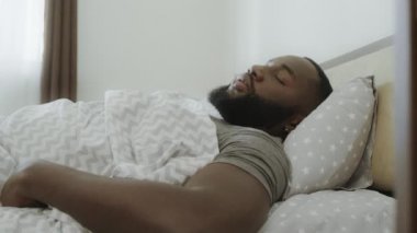 Sabah yatakta oturan şok siyah adam. Genç Yetişkin yatak telefon alıyor