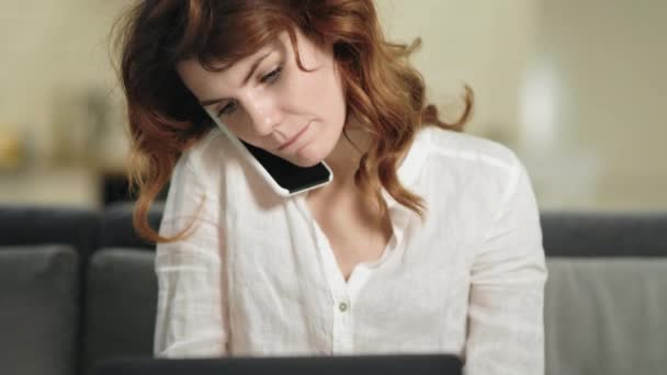 Mujer sonriente sentada con portátil en el lugar de trabajo. Mujer de negocios hablando por teléfono — Vídeo de stock