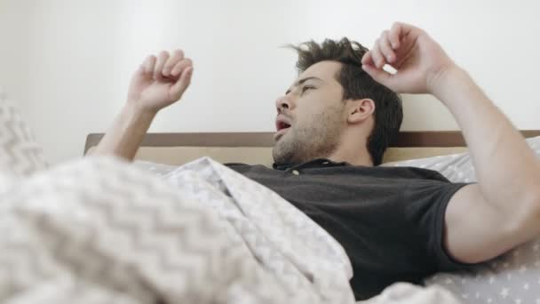 Спящий мужчина зевает на кровати по утрам. Красивый парень, растянувшийся в спальне . — стоковое видео