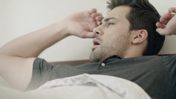 Un hombre guapo despertando por la mañana. Hombre feliz estirándose en la cama en casa . — Vídeos de Stock