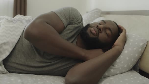 Zwarte man slapen bed in de ochtend. Jonge mannelijke persoon die zich langzaam in bed uitstrekt. — Stockvideo