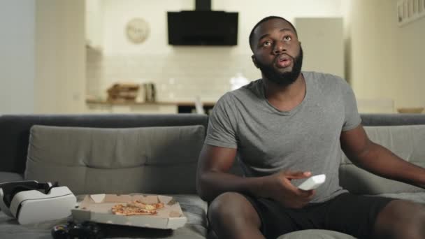 Hombre africano buscando programa de televisión en casa. Sonriente hombre leyendo el mensaje en el teléfono — Vídeos de Stock