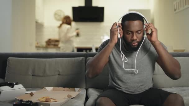 Sorpreso uomo nero ascoltare musica a casa cucina con auricolari . — Video Stock