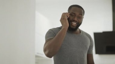 Gülümseyen siyah adam evde telefon konuşuyor. Akıllı telefon ile ayakta genç adam