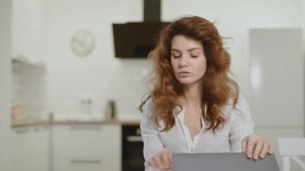 Mujer seria tomando el teléfono en la cocina abierta. Jovencita cerrando laptop en casa . — Vídeos de Stock