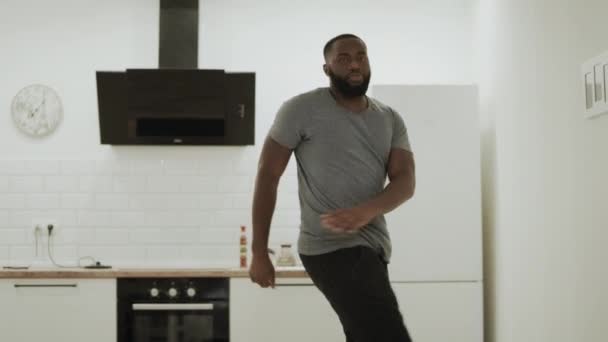 Χαρούμενος μαύρος άντρας που χειροκροτάει τα χέρια του στην ανοιχτή κουζίνα. Ευτυχισμένος νέος τύπος χορεύει στο σπίτι — Αρχείο Βίντεο