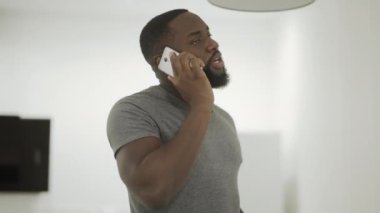 Ciddi siyah adam evde mutfakta telefon konuşuyor. Genç adam konuşan Smartphone