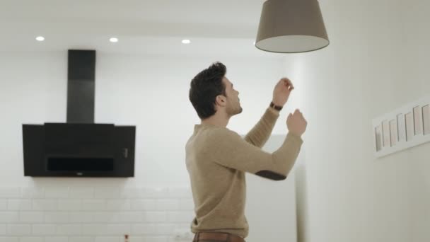 Hombre blanco desenroscar bombilla en la cocina abierta. Tipo parado debajo de la araña — Vídeo de stock