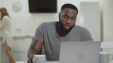 Açık mutfakta konsantre siyah adam çalışma laptop bilgisayar.