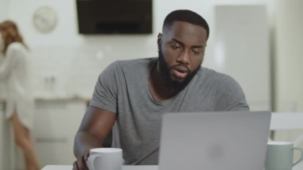 Geconcentreerde zwarte man werkende laptop computer in open keuken. — Stockvideo