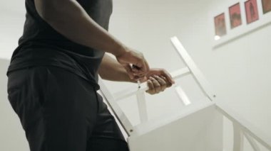 Siyah adam elleri mutfakta sandalye tutuyor. Ahşap sandalye tamir closeup eller.