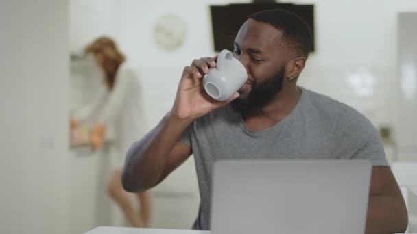 Lachen zwarte man drinken van thee in open keuken. Witte vrouw schoonmaken tabel — Stockvideo