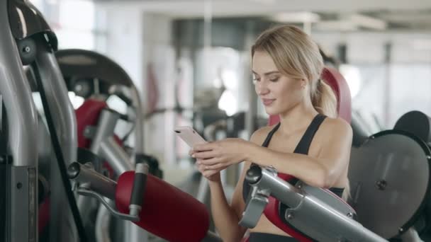 Mujer fitness relajante con teléfono móvil en el gimnasio deportivo . — Vídeo de stock