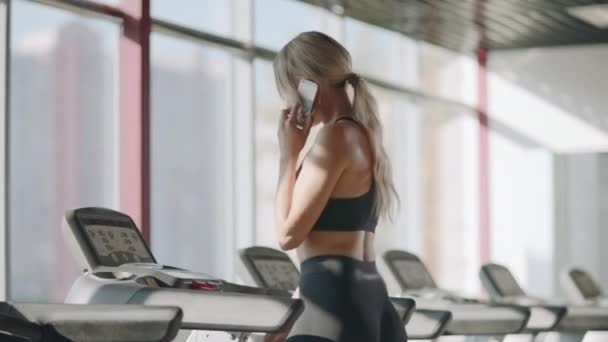 Fitness kvinna gå på löpbandet i gym Club. Pretty Girl ringer mobiltelefon — Stockvideo