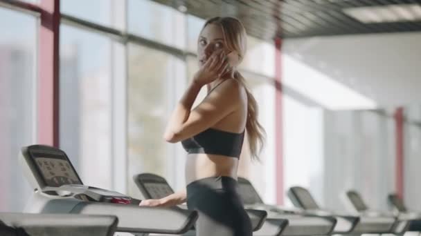 Slim Sport kobieta rozmawia telefon komórkowy w siłowni fitness. Fit dziewczyna Walking bieżni — Wideo stockowe