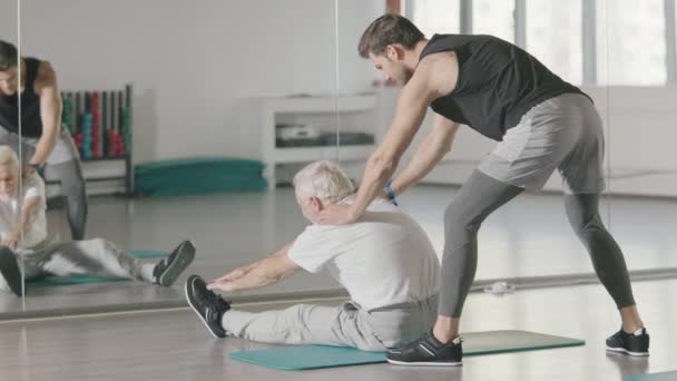 Senior man doet stretching oefening voor spiegel in de sportschool. — Stockvideo